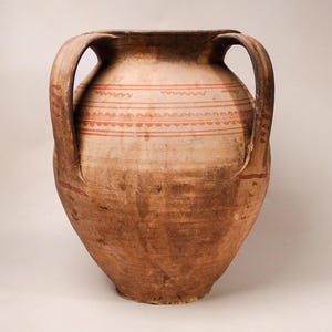 May include: A large, tan, earthenware vessel with two prominent side handles. The upper body features horizontal bands of red painted patterns, including wavy lines and repeating semi-circles. The surface has a weathered, textured appearance.