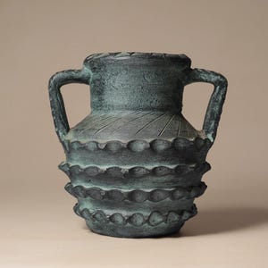 May include: A dark teal and black vase with two side handles, featuring a textured surface with horizontal rows of raised, scalloped ridges and a series of diagonal etched lines around the upper neck area, finished with a weathered patina.