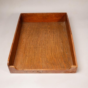 May include: A rectangular wooden tray with a medium brown finish and visible wood grain patterns. The tray features four high sides, with the front side having a lower, U-shaped cutout section for easy access to the interior base of the tray.