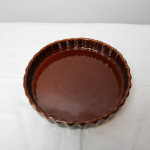 Puede incluir: Una fuente para tarta de cerámica marrón con borde ondulado. El plato tiene un acabado brillante y una forma circular. El plato para tarta está diseñado para hornear y servir tartas y quiches. El plato mide aproximadamente 25 cm de diámetro.