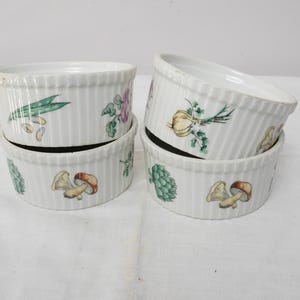 Puede incluir: Juego de seis ramequines de cerámica blanca con lados acanalados verticales. Cada ramequín presenta un diseño de verdura pintado a mano, incluyendo champiñones, alcachofas y cebollas. Ideales para hornear porciones individuales. Miden unos 10 cm de diámetro.