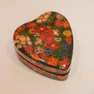 May include: A heart-shaped trinket box with a floral design. The box is covered in a colorful pattern of red, orange, pink, blue, and yellow flowers with green leaves. The box is made of a glossy material.
