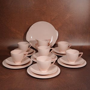Puede incluir: Un juego de vajilla rosa pálido que incluye una fuente grande, una jarra para crema y cuatro servicios de mesa. Cada servicio consta de una taza, un platillo y un plato. Las piezas presentan un acabado liso de color sólido.