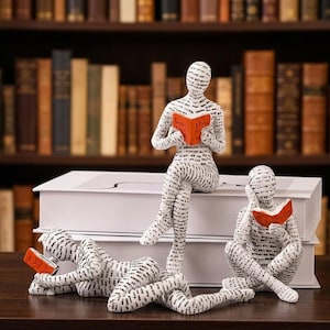 May include: Three white figurines of people reading books. The figures are covered in black text and hold orange books. One figure sits, one reclines, and one is seated. A bookshelf filled with books forms the background.