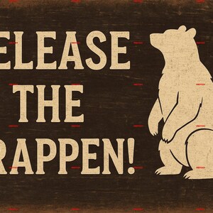 Può includere: Un cartello in legno rustico con la scritta "RELEASE THE CRAPPEN!" in un font vintage. Una silhouette di orso color crema è a destra. Lo sfondo è marrone scuro, conferendo un aspetto rustico e invecchiato.