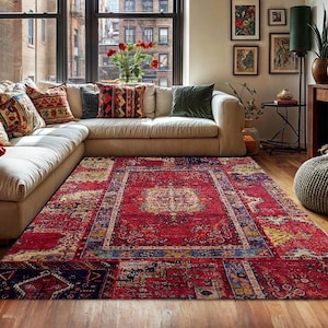 Peut inclure: Un tapis rouge rectangulaire orné d'un motif complexe est au centre de la pièce. Le tapis présente un médaillon central et des bordures bleues, jaunes et crème. Il est placé dans un salon avec un canapé d'angle crème.