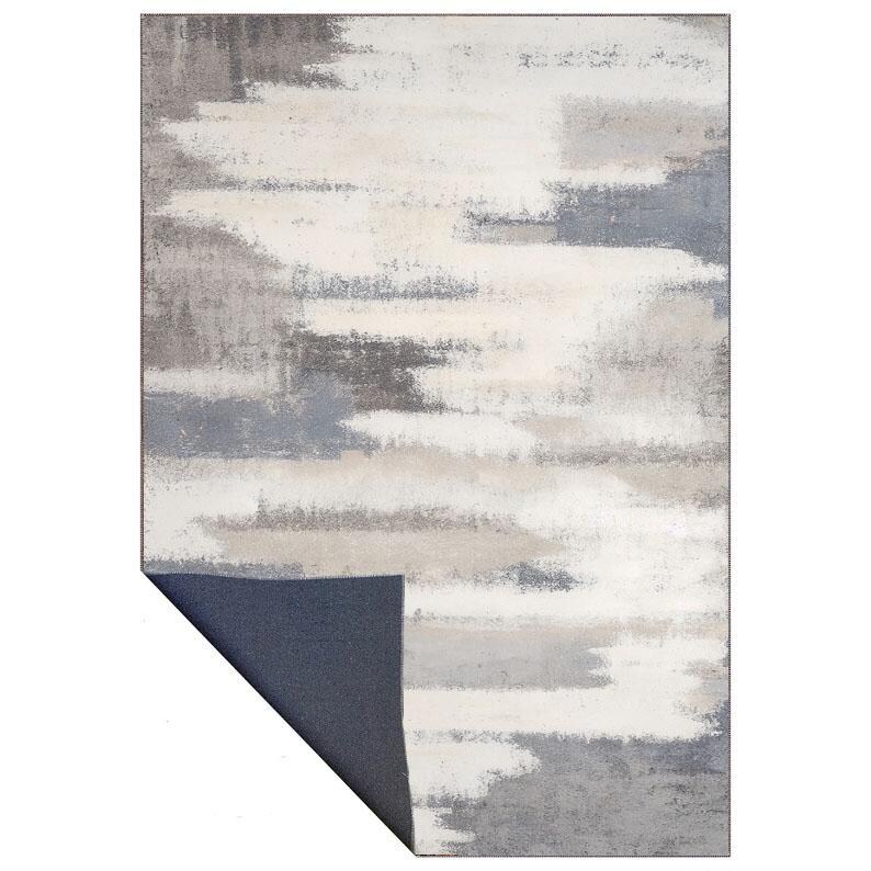 May include: A rectangular area rug with an abstract design. The rug features a pattern of horizontal brushstrokes in shades of white, gray, and blue. The bottom left corner is folded back, revealing a dark blue backing.