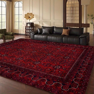 May include: A large, rectangular red rug with a detailed, dark pattern. The rug dominates a living room, with a black leather sofa and a green armchair visible. The rug's design features geometric shapes and floral motifs, adding a touch of elegance.