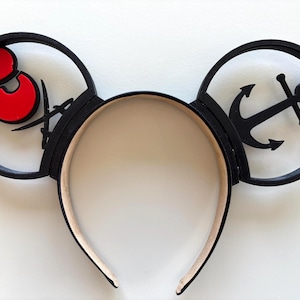 May include: Black Mickey Mouse ears headband with a red Mickey Mouse silhouette on one ear and a black anchor silhouette on the other ear.