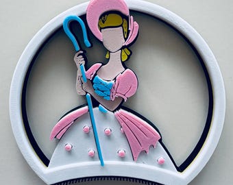 May include: A 3D-printed Bo Peep character from Toy Story, featuring a pink bonnet, dress, and staff. The character is set within a white circular frame with a black border. The design is a colorful, cartoon-style depiction.