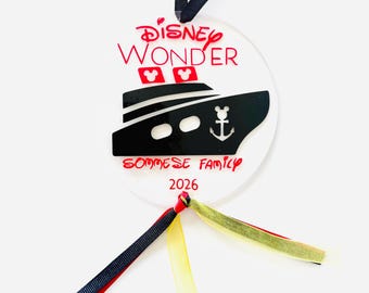 May include: A clear, round ornament with the words "Disney Wonder" in red, and a black ship illustration. The ornament includes the text "SOMMESE FAMILY 2026" and has a navy blue ribbon for hanging, plus red, yellow, and gold ribbons.