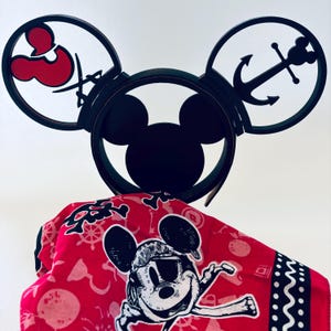 May include: Black Mickey Mouse ear headband with cut-out designs of an anchor and a pirate symbol. A red bandana with a Mickey Mouse graphic and nautical patterns is draped below the headband.