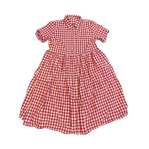 Op de afbeelding: Een rood-witte geruite jurk met korte mouwen en een knoopsluiting aan de voorkant. De jurk heeft een kraag en een gelaagde rok. De stof heeft een klassiek ruitpatroon, perfect voor een casual zomerse look.