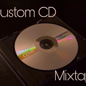 May include: A black CD case with a silver CD-R disc inside. The disc has a rainbow iridescent sheen and the text "Maxell CD-R 80-700" printed on it. The text "Custom CD Mixtape" is printed on the case.