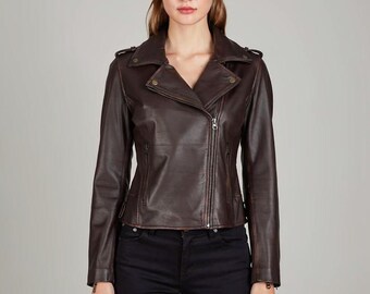 May include: A brown leather jacket with a classic asymmetrical zipper closure. The jacket features a notched collar, shoulder epaulets, and zippered pockets. The model is wearing black jeans. The jacket appears to be made of high-quality leather.