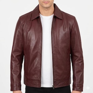 May include: A deep burgundy leather jacket featuring a classic point collar, a full-length front zipper closure, long sleeves with buttoned cuffs, and two vertical side pockets. The jacket is worn over a plain white crew neck t-shirt.