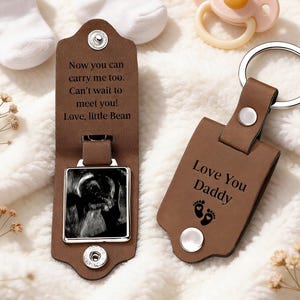 May include: Two brown leather keychains, one with a baby ultrasound photo and the text "Now you can carry me too. Can't wait to meet you! Love, little Bean." The other keychain says "Love You Daddy" with footprints.