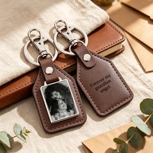 May include: Two brown leather keychains with silver metal hardware. One keychain features a rectangular black and white photograph of two people. The other keychain is engraved with the text, Forever my guardian angel, in a dark sans-serif font.