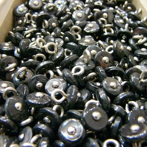 May include: A close-up image of a large quantity of black buttons with silver loops. The buttons are arranged in a random pattern and appear to be made of a smooth, shiny material.