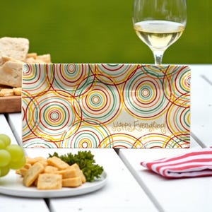 May include: Rectangular serving platter with a cream background and colorful overlapping circles in red, yellow, green, and orange. The words "Happy Everything!" are written in gold script. The platter is on a white table with food and a glass of wine.