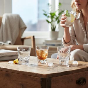 Könnte beinhalten: Mehrere klare Trinkgläser mit Muster auf einem Holztisch, einige gefüllt mit Eis und Getränken. Ein Glas trägt den Text "LSA". Eine Person hält ein Glas mit einer Zitronen- und Minz-Garnitur.