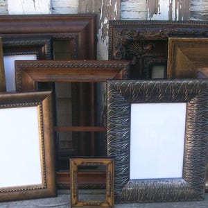 May include: A collection of rectangular picture frames in various sizes and finishes, including dark wood, metallic bronze, and textured black. The frames feature diverse border designs, some with beaded edges and others with intricate patterns.