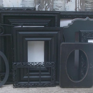 May include: A collection of various black picture frames in different shapes and sizes, including rectangular, oval, and ornate styles. Some frames feature intricate carved details, while others have smooth edges or metal mesh accents.