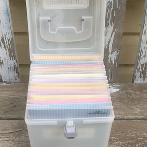 May include: A clear plastic storage box with a hinged lid and a handle, featuring the text Close To My Heart. Inside are multiple dividers holding pastel-colored paper sheets with striped and dotted patterns. One sheet is labeled A1080 Amore Numbers.