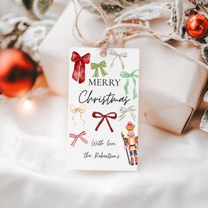 May include: A gift tag with watercolor illustrations of bows in red, green, and gold, with the words "MERRY Christmas" in elegant script. A small illustration of a nutcracker is also included. The tag is tied to a wrapped gift.