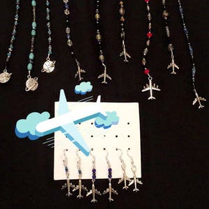 May include: A set of nine silver airplane charms on black beaded chains and earrings. The chains are attached to a black fabric background. The earrings are displayed on a white card with a blue airplane graphic.