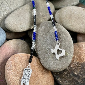 May include: Two beaded necklaces with charms. One charm is a boot and the other is the state of Texas with a heart cut out. The beads are black, blue, and clear.