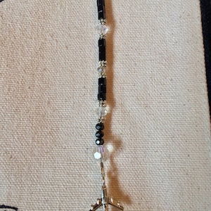 May include: A black and silver beaded bookmark with a small airplane charm at the end. The beads are black and clear.