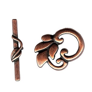 May include: Copper-toned metal clasp with a floral design. The clasp has a decorative loop and a straight bar with a leaf design.