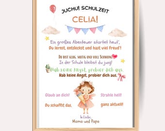 May include: A framed print with a light wood border. The print features the text "JUCHU! SCHULZEIT CELIA!" and other German text with illustrations of a balloon, clouds, stars, and a fairy. The print is a colorful, whimsical design.