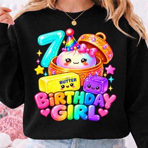 Puede incluir: Una sudadera negra con un gráfico colorido que muestra el número siete, una bola de masa kawaii en una vaporera dorada, una barra de mantequilla con la etiqueta BUTTER y un cubo morado. El texto BIRTHDAY GIRL está en letras brillantes.