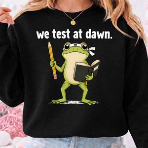 May include: A white ceramic mug with a black handle and the text "But First, Coffee" in a black, handwritten-style font. The mug is on a white surface.