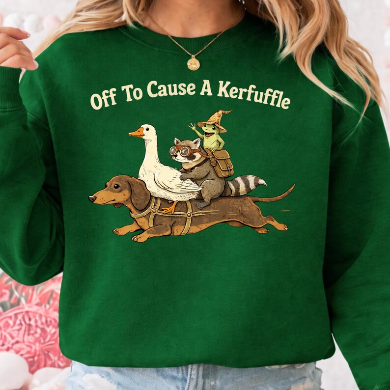 K&ouml;nnte beinhalten: Dunkelgr&uuml;nes Sweatshirt mit dem wei&szlig;en Schriftzug "Off To Cause A Kerfuffle". Die Grafik zeigt einen Dackel, der eine wei&szlig;e Gans, einen Waschb&auml;ren mit Brille und einen Frosch mit Hexenhut tr&auml;gt.