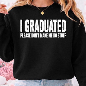 Könnte beinhalten: Schwarzes Sweatshirt mit dem weißen Text "I GRADUATED PLEASE DON'T MAKE ME DO STUFF". Das Sweatshirt hat einen Rundhalsausschnitt und lange Ärmel. Eine goldene Halskette mit Anhänger ist sichtbar.