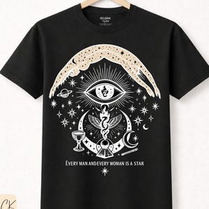 May include: Black t-shirt with a white graphic design featuring an eye, stars, and crescent moons. The text "EVERY MAN AND EVERY WOMAN IS A STAR" is printed below the design. The shirt is made of premium cotton.
