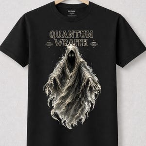 May include: Black t-shirt featuring a spectral figure with glowing eyes and a flowing cloak. The text "QUANTUM WRATH" is displayed above the figure in a stylized font. The shirt is hanging on a wooden hanger.