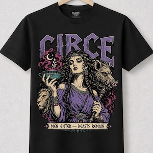 Può includere: Una t-shirt nera a maniche corte con una stampa grafica di una donna che tiene una ciotola con fumo viola, un leone e un cinghiale. Il testo recita CIRCE in alto e MEN ENTER - BEASTS REMAIN in basso su un nastro, con toni viola e beige.
