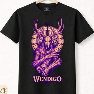Puede incluir: Camiseta negra con un diseño morado de Wendigo. El diseño incluye una calavera con cuernos, un patrón circular y la palabra "WENDIGO". La camiseta está hecha de algodón premium.