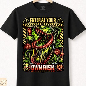 Könnte beinhalten: Schwarzes T-Shirt mit einer Grafik einer fleischfressenden Pflanze und dem Text "ENTER AT YOUR OWN RISK". Das Design beinhaltet einen Totenkopf, ein Biohazard-Symbol und Zielsymbole. Das Shirt ist aus Premium-Baumwolle.