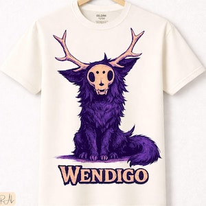 Puede incluir: Camiseta de color crema con un diseño de Wendigo morado. El gráfico muestra una criatura con cuernos y una cara de calavera. La palabra "WENDIGO" está impresa en morado debajo de la imagen. La camiseta está hecha de algodón natural de primera calidad.