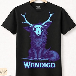 Puede incluir: Camiseta negra con una ilustración de Wendigo morado y azul. El diseño incluye una calavera, cuernos y la palabra "WENDIGO" en azul. Hecha de algodón premium.