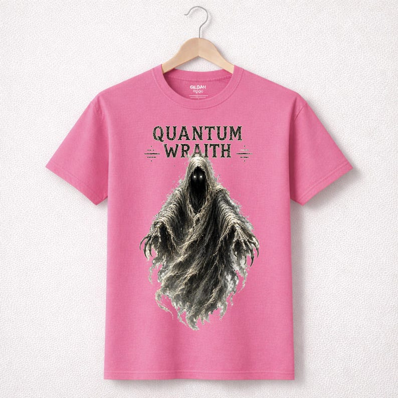 以下が含まれることがあります： 「QUANTUM WRAITH」の文字と、光る目とぼろぼろのマントを着たフード付きの人物のイラストが描かれたピンク色のTシャツ。Tシャツは木製のハンガーに掛けられています。デザインはファンタジーまたはホラーをテーマにしている可能性があります。