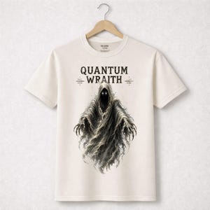 以下が含まれることがあります： オフホワイトのTシャツ。フード付きの人物が、光る目と爪のある手で描かれています。「QUANTUM WRAITH」の文字がゴシック体で人物の上に印刷されています。木製のハンガーにTシャツが掛けられています。
