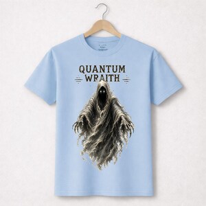 以下が含まれることがあります： 「QUANTUM WRAITH」の文字と、光る目と伸びた爪を持つ幽霊のような人物の詳細なイラストが描かれた、水色のTシャツ。 デザインはTシャツの中央に配置されています。