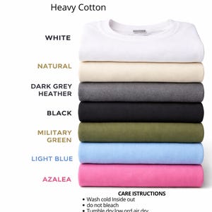 以下が含まれることがあります： GILDAN 5000 Heavy CottonのTシャツのスタック。白、ナチュラル、ダークグレーヘザー、黒、ミリタリーグリーン、ライトブルー、アザレアなど、さまざまな色があります。お手入れ方法がシャツの下に記載されています。