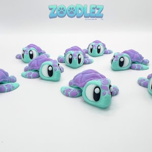 May include: A collection of colorful turtle figurines. Each turtle has a purple shell, a light blue body, and large white eyes with black pupils. The image includes the text "Zoodlez" in blue.